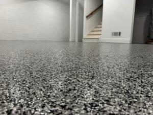 Dark gray, black and white flake basement floor coating with staircase in background