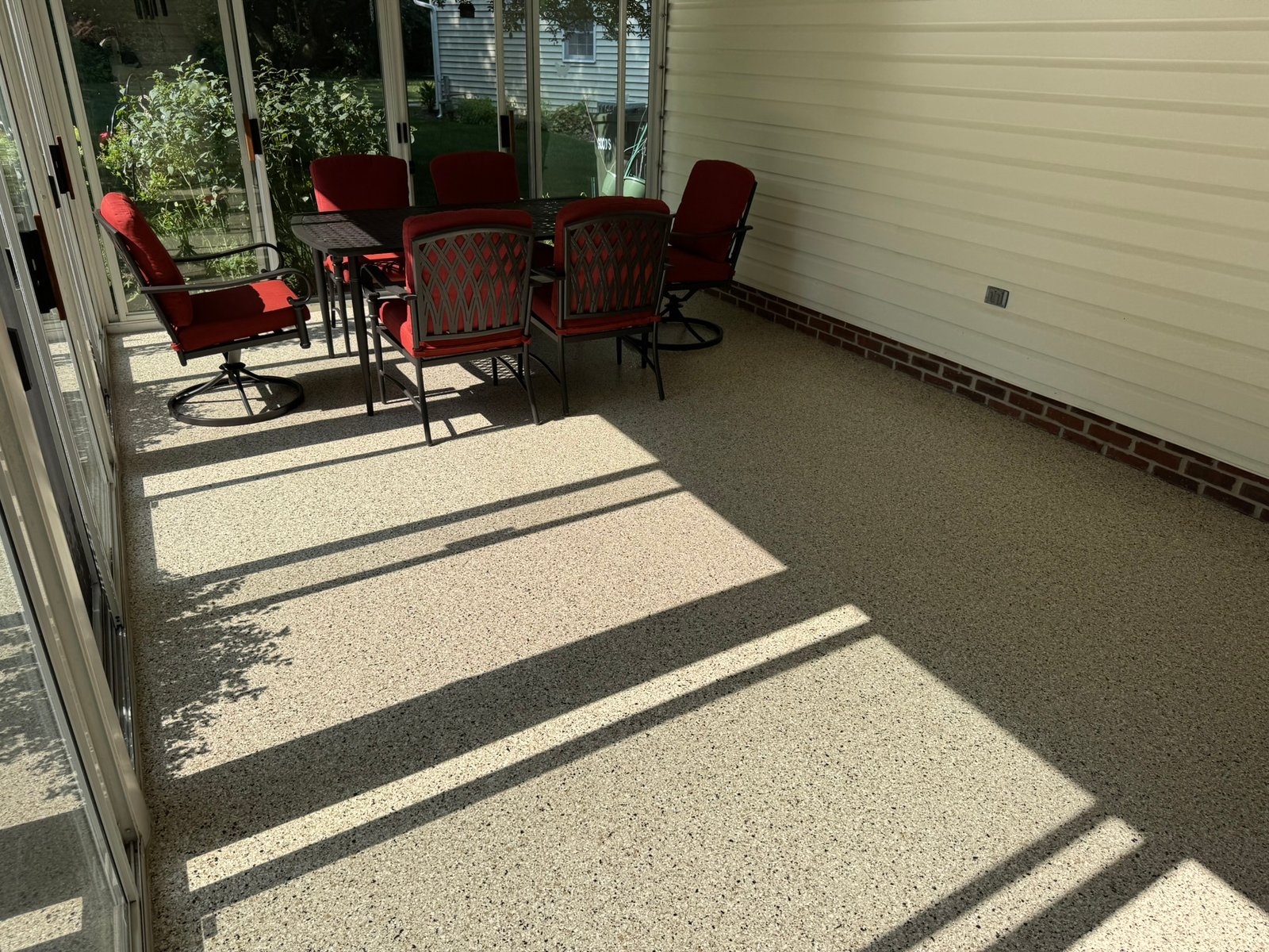 Furnished sunroom with patio table and red cushioned chairs on flake-coated floor