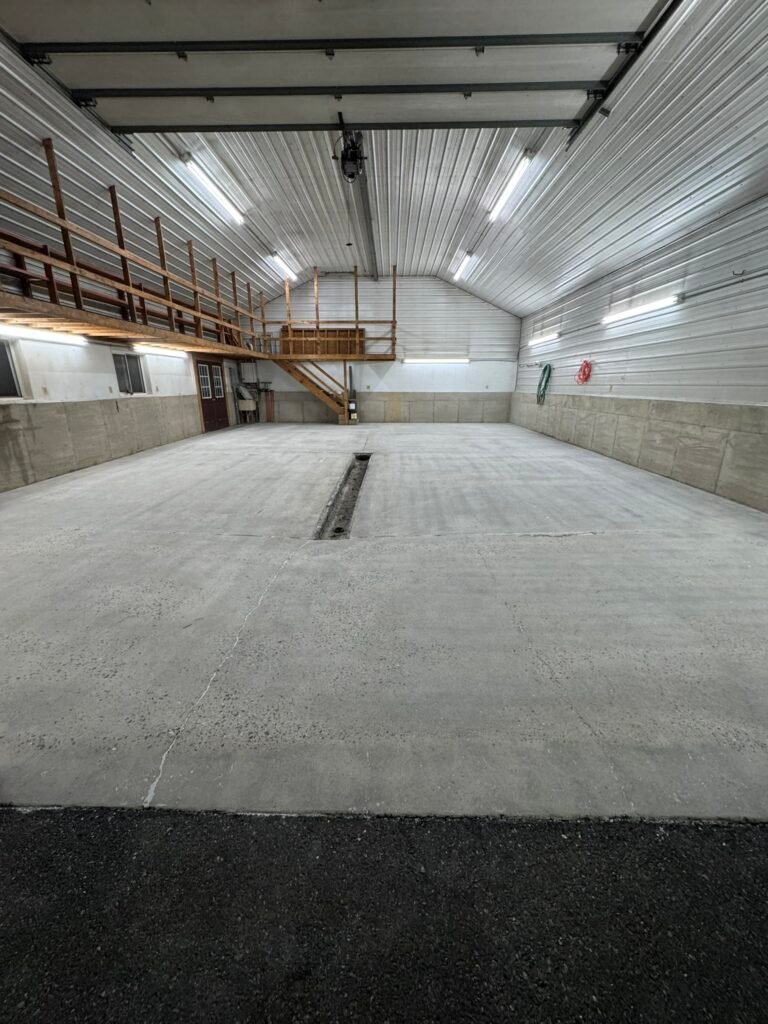 Bare concrete floor in large pole-barn building before coating, mezzanine storage loft above