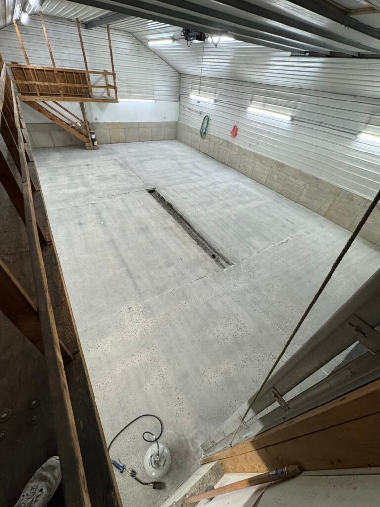 Elevated view of bare concrete pole-barn floor and wooden mezzanine before coating