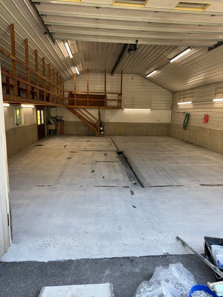 Bare concrete pole-barn floor before coating, showing drain channel and cracks