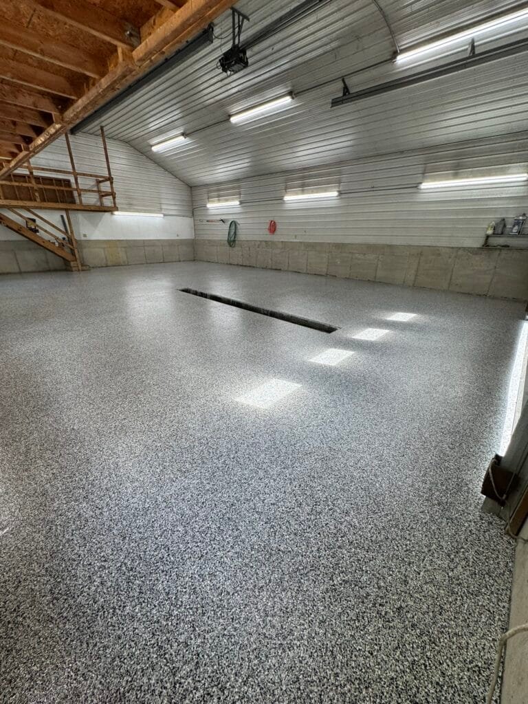 Finished gray, black and white flake pole-barn floor coating under metal roof trusses
